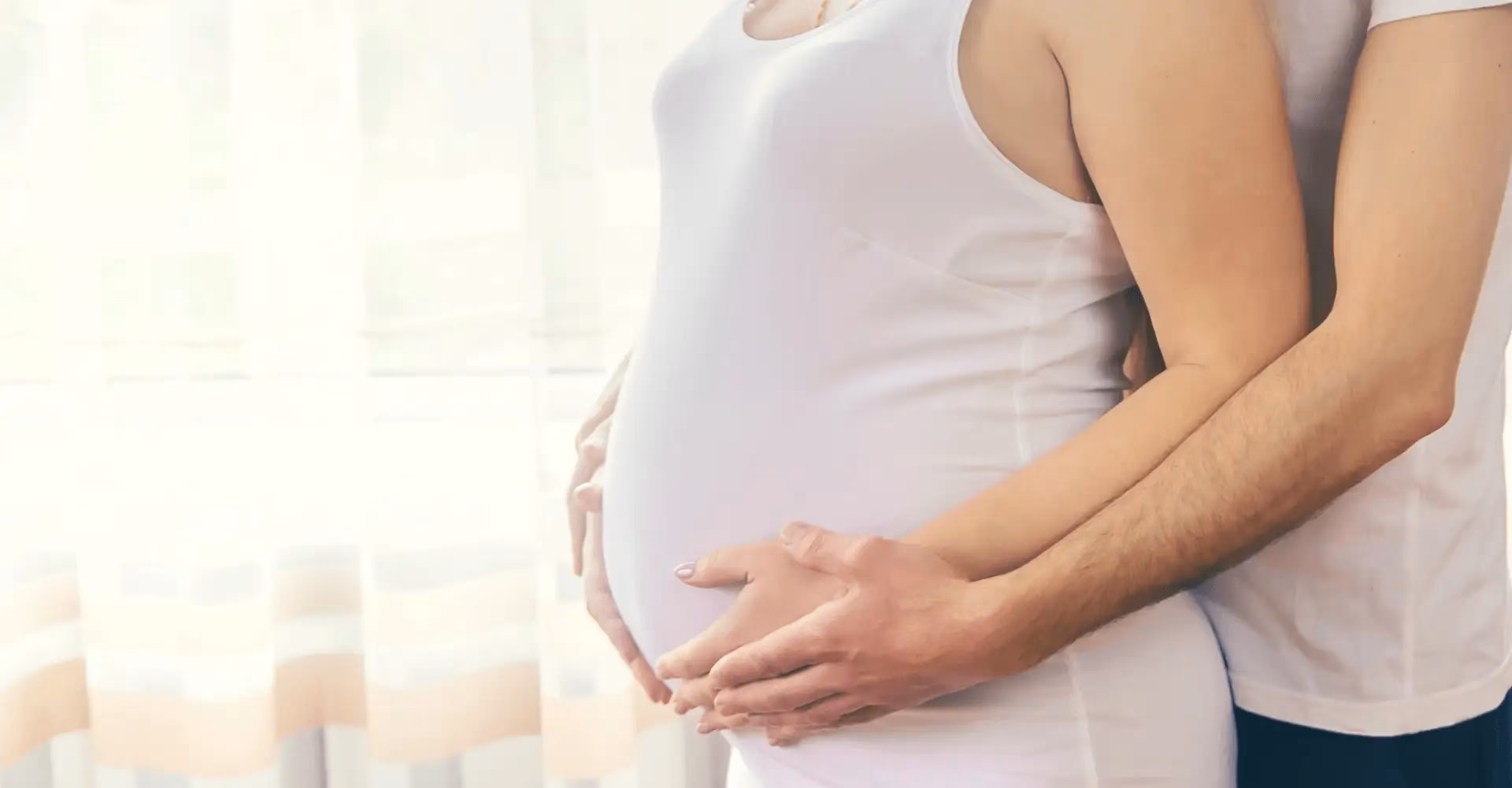 Pregnant woman with the arms of her spouse around her.